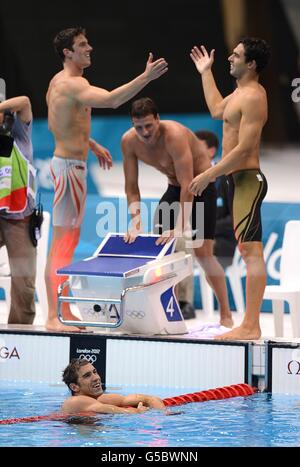 Die USA Michael Phelps (im Pool), Conor Dwyer (links), Ryan Lochte (Mitte) und Ricky Berens (rechts) feiern, nachdem sie am vierten Tag der Olympischen Spiele 2012 in London das 4 x 200 m Freistil-Relay-Finale im Aquatics Center im Olympiapark gewonnen haben. Stockfoto