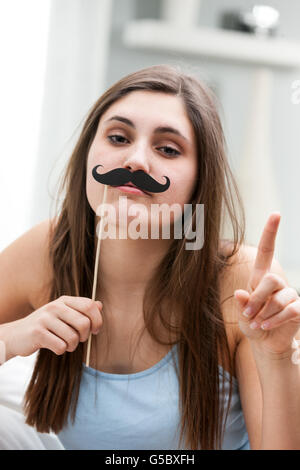 Verspielte junge Frau mit einem falschen Schnurrbart Foto Stand Zubehör hält es an ihre Lippen und heben den Finger mit einer schweren involviert Stockfoto