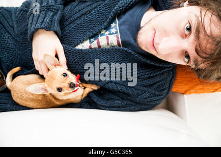 Porträt eines jungen Mannes mit einem Chihuahua liegend auf dem Sofa und starrte auf Kamera Stockfoto