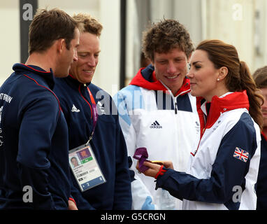 Der britische Finn-Goldmedaillengewinner Ben Ainslie zeigt der Herzogin von Cambridge seine Goldmedaille, während der Lasersegler Paul Goodison und der 470-Segler Stuart Bithell heute die olympische Segelstätte in Weymouth betrachten. Stockfoto