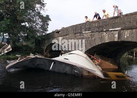 Maria ward (ganz links) und Freunde blicken auf ihre Karawane, die über eine Meile Bach vom Bryn Gwyn Ferienpark in der Nähe von Bala, Nordwales, durch eine Sturzflut gespült wurde. Bis zu 45,000 Häuser in Mittel- und Südwales waren ohne Strom. *... zumindest für einen Teil des Tages nach den Nächten Stürmen. Stockfoto