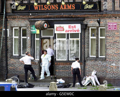 Polizeibeamte suchen im Wilsons Arms Pub in Leeds nach, wo ein Familienvater niedergeschossen wurde, während Kinder Party-Spiele spielten. Der frühere Profi-Rugby-League-Star David Nelson, 38, wurde am 22/07/01 im Pub in Seacroft in den Kopf geschossen. *...auf der rechten Seite sind Floral Tributes an Herrn Nelson angehäuft. Stockfoto