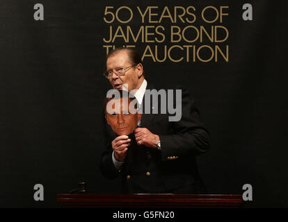 Sir Roger Moore hält eine Maske des aktuellen James-Bond-Schauspielers Daniel Craig bei Christie's 50 Years of James Bond Sale, mit Erinnerungsstücken, die von der Bond-Besetzung gespendet wurden, in Christie's in South Kensington, London. Stockfoto