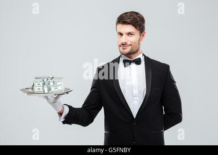 Wunderschöne junge Butler im Smoking stehen und halten Tablett mit Geld Stockfoto