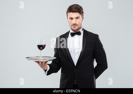 Porträt des jungen Kellner im Smoking mit Glas Rotwein auf silbernen Tablett Stockfoto