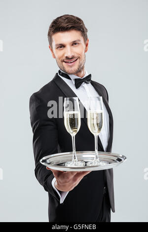 Lächelnde junge Kellner im Smoking bietet Ihnen Glas Champagner Stockfoto