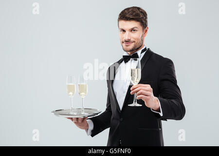 Attraktive junge Kellner im Smoking mit Tablett und Glas Champagner Stockfoto