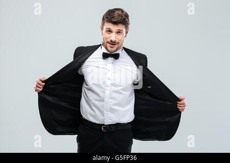 Lächelnder junge Mann im Smoking mit Fliege seine Jacke ausziehen Stockfoto