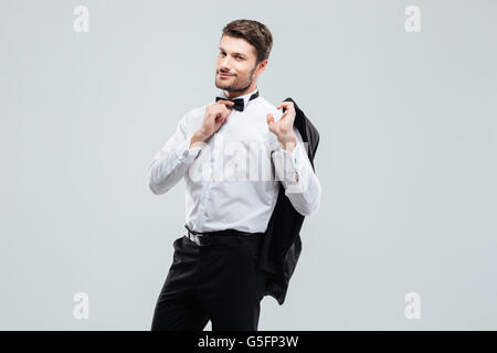 Attraktive junge Mann im Smoking hält seine Jacke Stockfoto