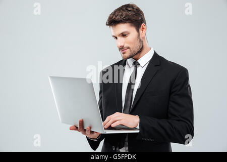 Hübscher junger Geschäftsmann stehend und mit Laptop auf weißem Hintergrund Stockfoto