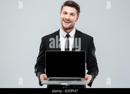 Glücklich attraktiver junger Geschäftsmann mit leeren Bildschirm Laptop über weißem Hintergrund Stockfoto