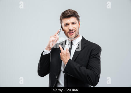 Verwirrt junger Geschäftsmann reden über Handy auf weißem Hintergrund Stockfoto