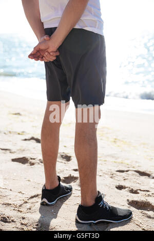 Nahaufnahme der Beine des jungen Mann in kurzen Hosen und Turnschuhe stehen am Strand Stockfoto