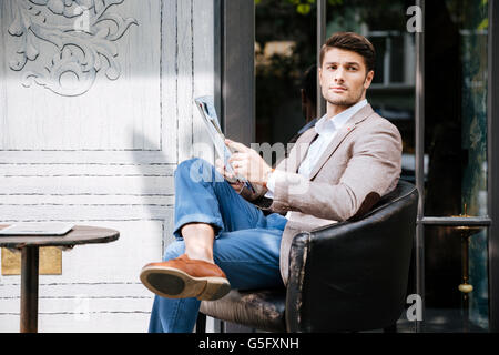 Nachdenklicher junger Mann sitzen und lesen Magazin im Café im freien Stockfoto