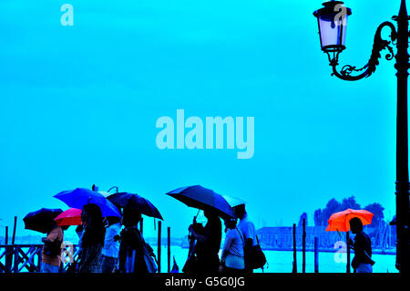 Touristen, die auf der Insel Venedig Italien, Regenschirme, Regen, Regenschirm rot. Kontur, Sonnenaufgang, verregneten Tag Stockfoto