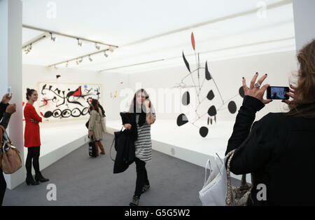 Die Besucher sehen einen Raum mit einem Gemälde von Joan Miro (links, der schmerzhafte Marsch unter der Führung des Flamboyant Bird of the Desert, 1968) und einer Skulptur von Alexander Calder (Triumphant Red, 1959-63) auf der Frieze Masters Kunstmesse im Regents Park im Zentrum von London. Stockfoto