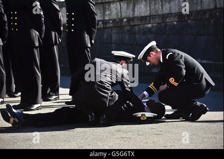 Marineoffiziere besuchen einen anderen Offizier, der während einer Passierparade am Britannia Royal Naval College in Dartmouth zusammenbrach, wo Premierminister David Cameron den Gruß nahm. Stockfoto