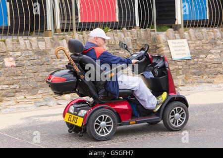 Älterer Mann auf der Mobilität Roller Elvis Fahrt vorbei an Reihe von Strandhütten auf Promenade in Bournemouth im Juni Stockfoto