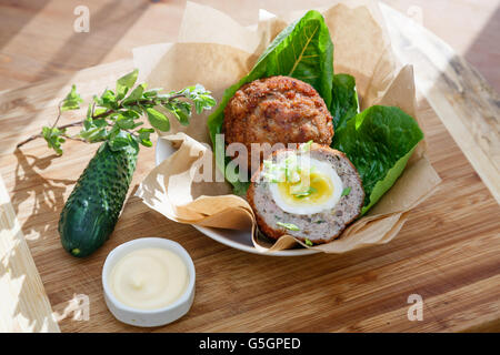 Schottische Eiern auf Kraftpapier mit Soße garnieren und Gurke cucmber Stockfoto