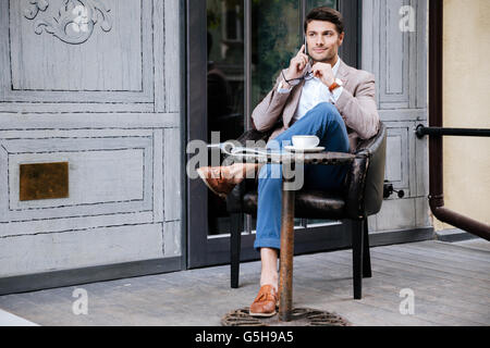 Nachdenklicher junger Mann sitzen und telefonieren mit Handy im Café im freien Stockfoto