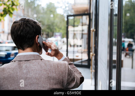 Rückansicht der junge Geschäftsmann gehen und reden über Handy in der Stadt Stockfoto