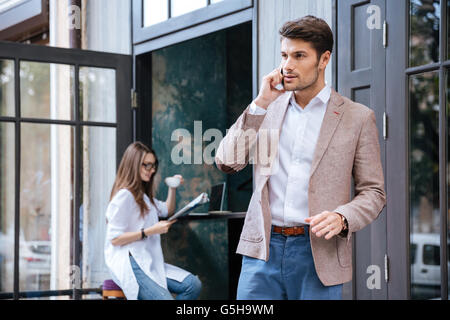 Attraktive junge stilvolle Geschäftsmann sprechen auf dem Handy draußen im café Stockfoto