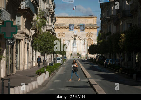 Lokalen Dame kreuzt die Rue Foch vor dem 17. Jahrhundert Arc de Triomphe in Montpellier, Südfrankreich. Stockfoto