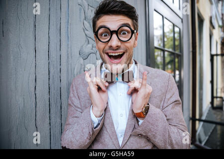 Porträt von fröhlich lustige junger Mann in runden Gläsern und hölzernen Bowtie stehen im freien Stockfoto