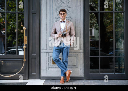 Voller Länge glücklich jungen Mannes in lustiger Runde Brille stehen und halten Sie alt Vintage Fotokamera Stockfoto