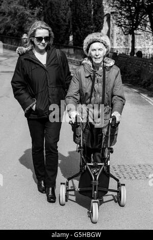 Einen weiblichen Verwandten zu Fuß mit einer behinderten älteren Frau mit einer drei-Rad Rollator, Sussex, UK Stockfoto