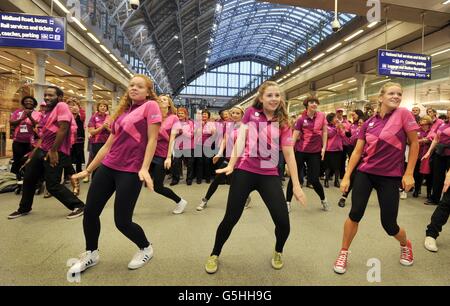 Eine Gruppe olympischer Freiwilliger tanzt während eines Flash-Mob am Eurostar-Terminal im Bahnhof St. Pancras in London, um ankommende Passagiere und die Öffentlichkeit zu unterhalten, da angekündigt wird, dass sie bei zukünftigen internationalen, sportlichen und touristischen Veranstaltungen in einer unterstützenden Rolle eingesetzt werden. Stockfoto