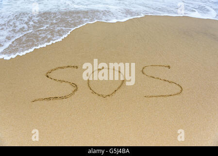 Wort-SOS am Strand vor dem Hintergrund der Meereswellen. Stockfoto