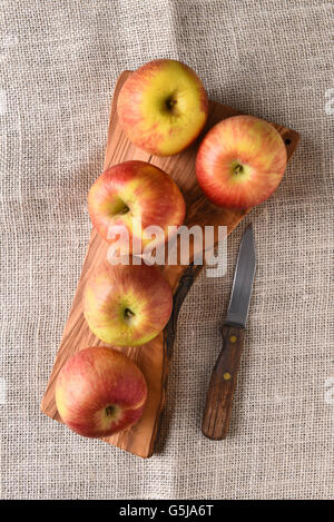 Vogelperspektive Blick auf eine Gruppe von Braeburn Äpfel auf ein Schneidebrett mit einem Messer auf einer Tischdecke Sackleinen. Stockfoto