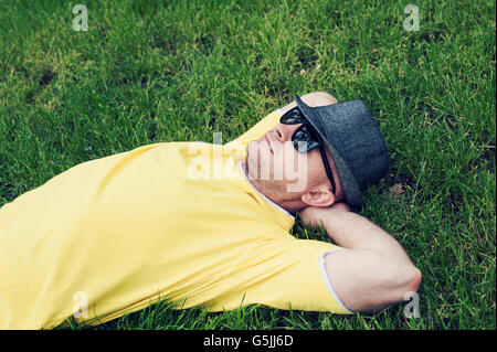 Mann in einem gelben T-shirt und Hut auf dem Rasen liegend Stockfoto