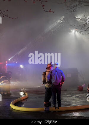 Chappaqua, NY - 11. April 2014:Mist umgibt Feuerwehrleute aus Chappaqua und mehreren umliegenden Städten im Westchester County New York kämpfen in einem Gebäude, in dem der Whispering Pines Flower Shop und die Wohnwohnungen in Chappaqua untergebracht sind, NY. Das Feuer begann gegen 1 UHR am Freitagmorgen und als die Morgendämmerung brach, ging das Feuer noch, wobei der starke Rauch die Umgebung rauchte. © 2014: Frau A. Campolongo Stockfoto