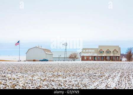 Amerikanische Flagge und Windmühle auf der Familienfarm in Licht abgestaubt Schnee im ländlichen Norden Osten Nebraska Stockfoto