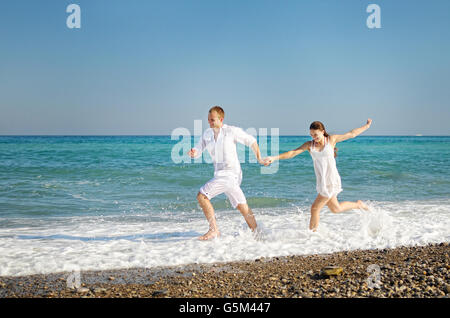 Glückliches junges Paar läuft, Hände an der Meeresküste beigetreten. Der Mann und ein Mädchen gekleidet in weißen Kleidern einfach. Auf Flächen expressio Stockfoto