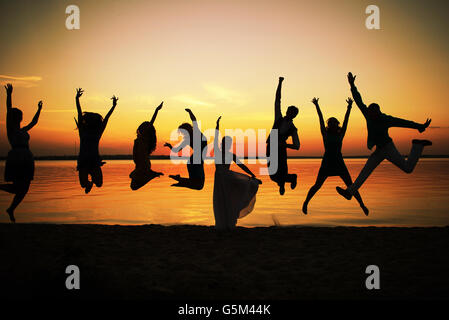 Silhouetten der Gruppe von Menschen in einem Sprung bei Sonnenuntergang. Acht junge Männer und Frauen in einen Sprung vor dem Abendhimmel dargestellt und die Stockfoto