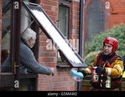 Ein Mitglied der Feuerwehr und Rettung von Nordwales übergibt einem Einwohner in St. Asaph, Denbighshire, Nordwales, Milch und eine Plastikbox, nachdem die Stadt über Nacht überschwemmt wurde. Stockfoto