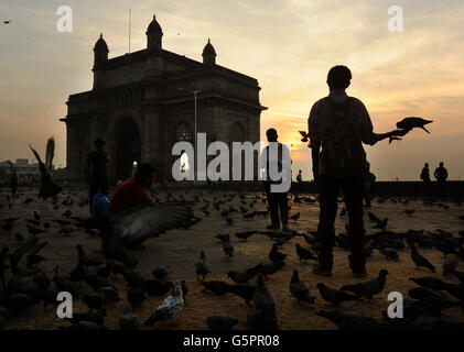 Ein Mann füttert Tauben, während die Sonne hinter dem Gateway of India im Apollo Bunder-Gebiet von Mumbai aufgeht, India PRESS ASSOCIATION Photo. Bilddatum: Donnerstag, 29. November 2012. Erbaut zum Gedenken an den Besuch von König George V und Königin Mary in Mumbai im Dezember 1911 (allerdings wurde nur ein Pappmodell der Struktur gesehen, da der Bau erst 1915 begann) Die letzten britischen Truppen, die Indien nach der Unabhängigkeit Indiens verlassen haben, durchzogen das Tor in einer Zeremonie am 28. Februar 1948 und signalisierten das Ende der britischen Herrschaft in Indien (British Raj). Bildnachweis sollte lauten: Anthony Stockfoto