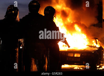 Die Bereitschaftspolizei steht neben einem ausgebrannten Auto, nachdem loyalistische Demonstranten Polizeilinien angegriffen hatten, im Osten von Belfast. Stockfoto