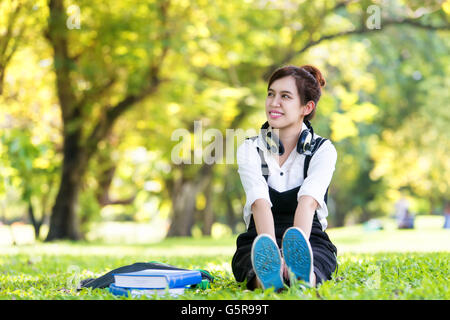 Junge Asiatin mit Kopfhörern hören Musik im Freien. Asiatische Frau Musik im Park genießen. Schöne asiatische Frau. Stockfoto