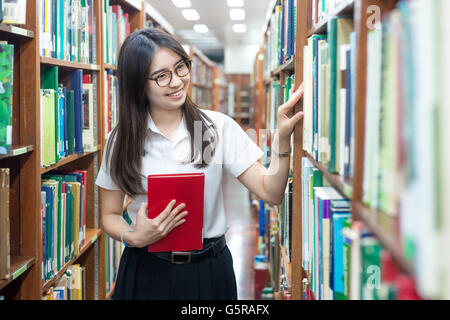 Asiatische Studentin in Uniform, die Lesung in der Bibliothek der Universität Stockfoto