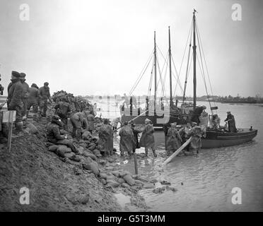 Militärangehöriger und Zivilisten entladen Sandsäcke von Fischerbooten, um den Hauptbruch in der Ostwand der Meeresabwehr von Canvey Island zu reparieren. Der morgendliche hohe Wasserstand war etwa einen Fuß höher als letzte Nacht und lag innerhalb von zweieinhalb Fuß von der Spitze der untersten Abschnitte der Wand entfernt. Stockfoto