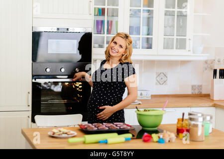 Schöne schwangere Frau Vorbereitung Muffins in Küche Stockfoto