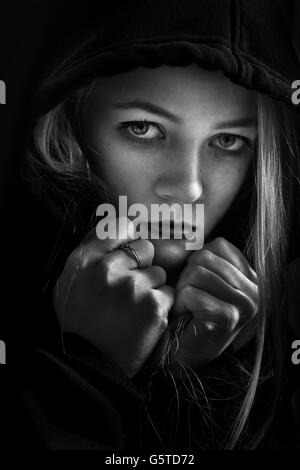 Angst vor Mädchen in Haube Blick in die Kamera auf schwarzem Hintergrund Monochrom Stockfoto