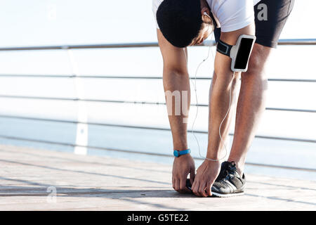 Entspannte afrikanischen Sportler stretching und Musikhören von leeren Bildschirm Smartphone am pier Stockfoto