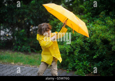 Kamerad in einem hellen gelben Regenmantel versucht, einen Regenschirm aus Wind Fehler halten. Er kleidete sich in einem hellen gelben Regenmantel. Großen dro Stockfoto