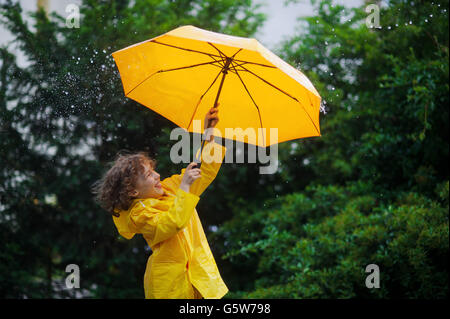 Kerlchen mit einem leuchtend gelben Regenschirm in den warmen Sommerregen. Er liebt den Regen und freut sich. Große Regentropfen fallen auf ein umbrell Stockfoto