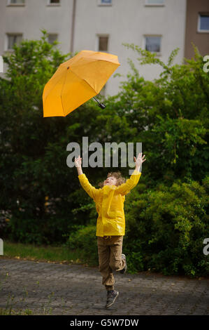 Die jungen von 8-9 Jahre in einem hellen gelben Regenmantel versucht, das scheidende gelben Dach fangen. Starker Wind hat ein Umb herausgezogen. Stockfoto